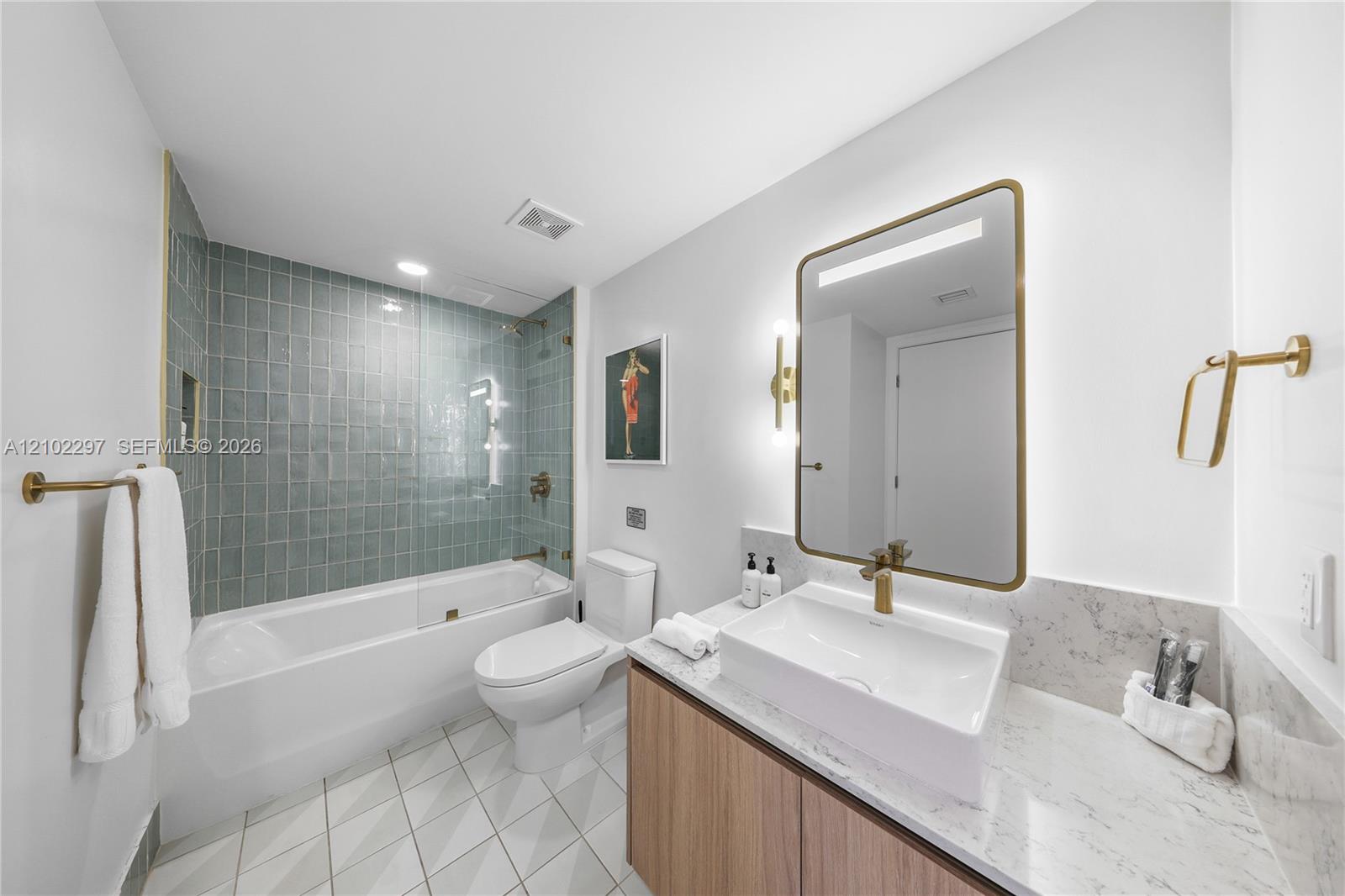 Bathroom with sage-green shower tile, a white tub, and a wood vanity with brass fixtures.