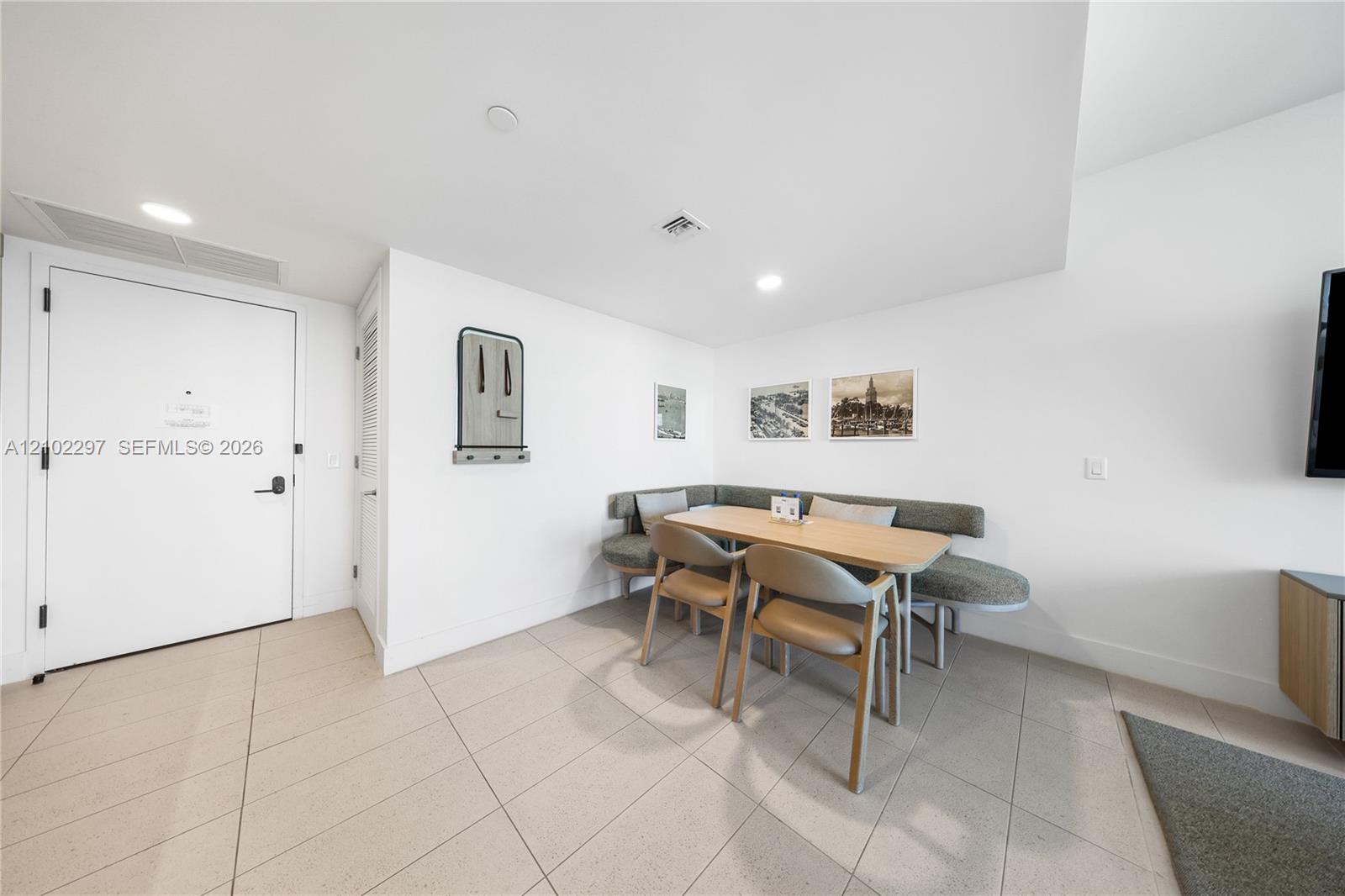 Dining nook with a wood table, chairs, gray corner banquette, and light tile floor.