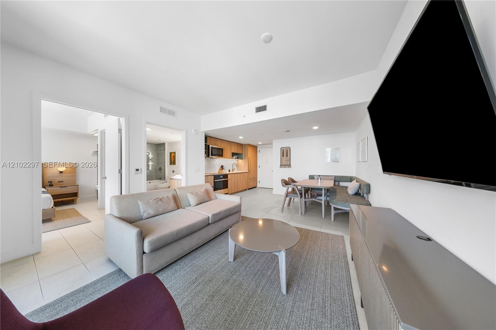 Open-plan condo living room with gray sofa, dining nook, and wood-cabinet kitchen.