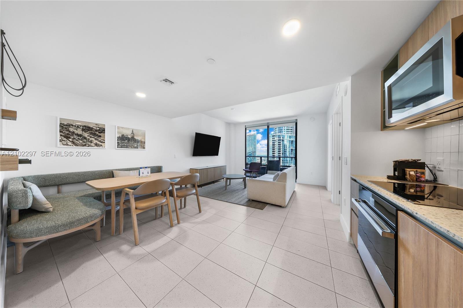 Open-plan living and dining area with gray sectional, kitchen, and high-rise city views.