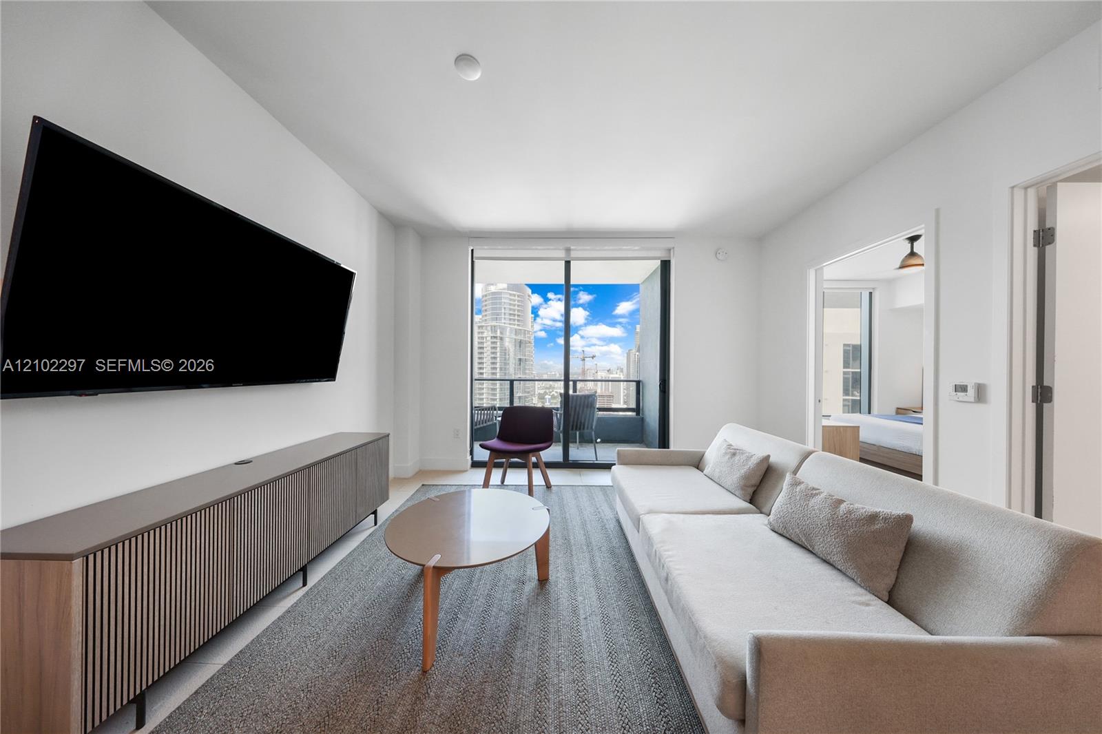 Furnished living room with a wall-mounted TV, balcony, and city skyline view.