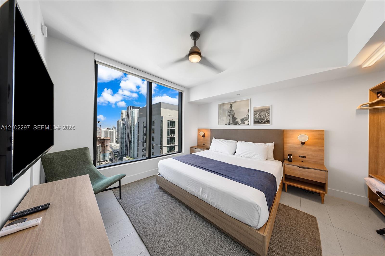 Furnished modern bedroom with a large window overlooking the city skyline.