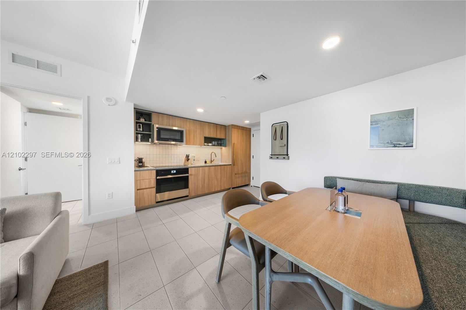 Furnished condo kitchen and dining area with wood cabinetry, tiled floor, and built-in appliances.