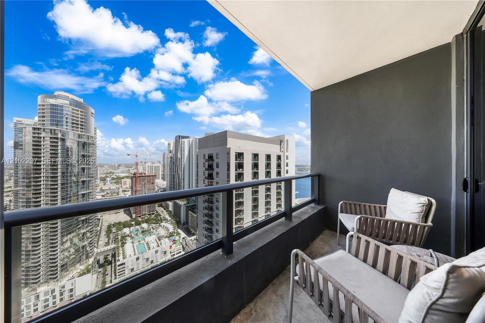 Balcony with cushioned chairs overlooking downtown Miami high-rises and water.