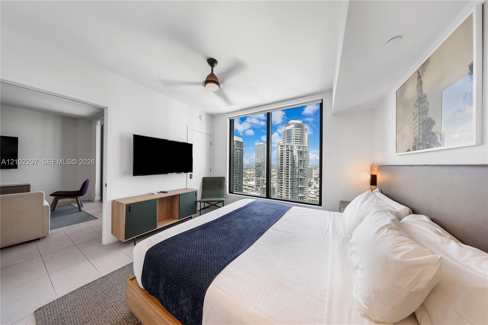 Furnished bedroom with a large window overlooking Miami high-rises and a navy bed runner.