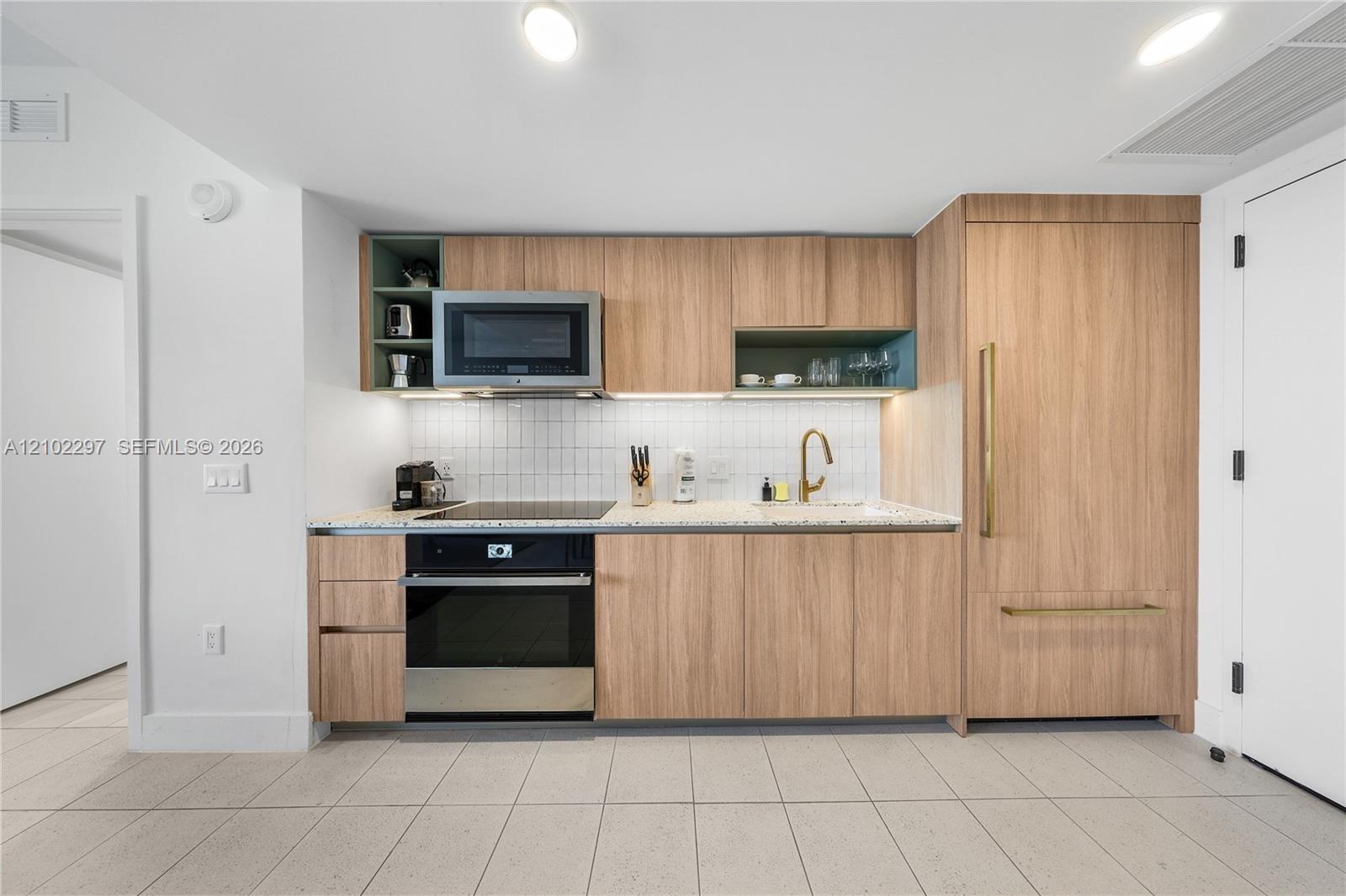 Modern kitchen with light wood cabinets, built-in appliances, and a brass faucet.