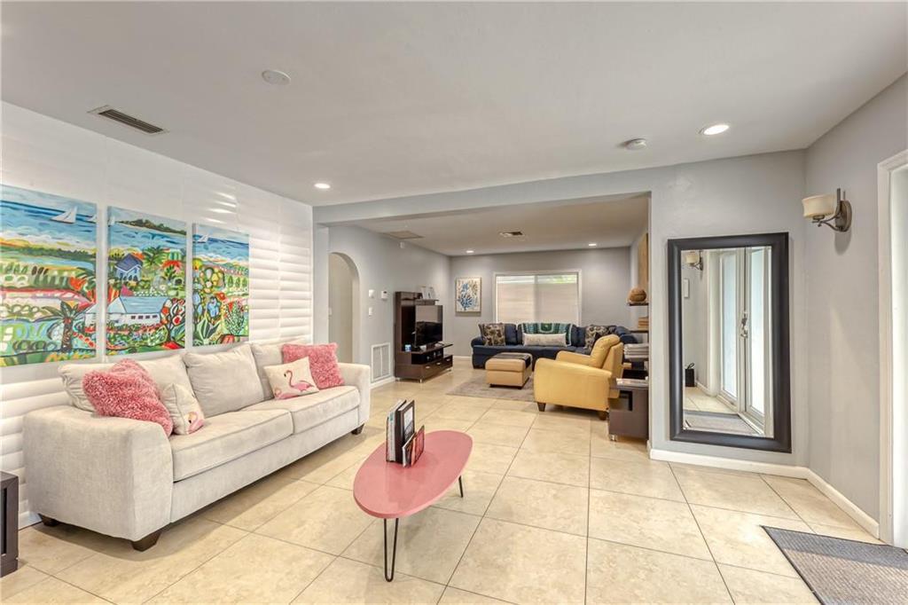 Living room with tropical wall art, a white sofa, and cream tile flooring.