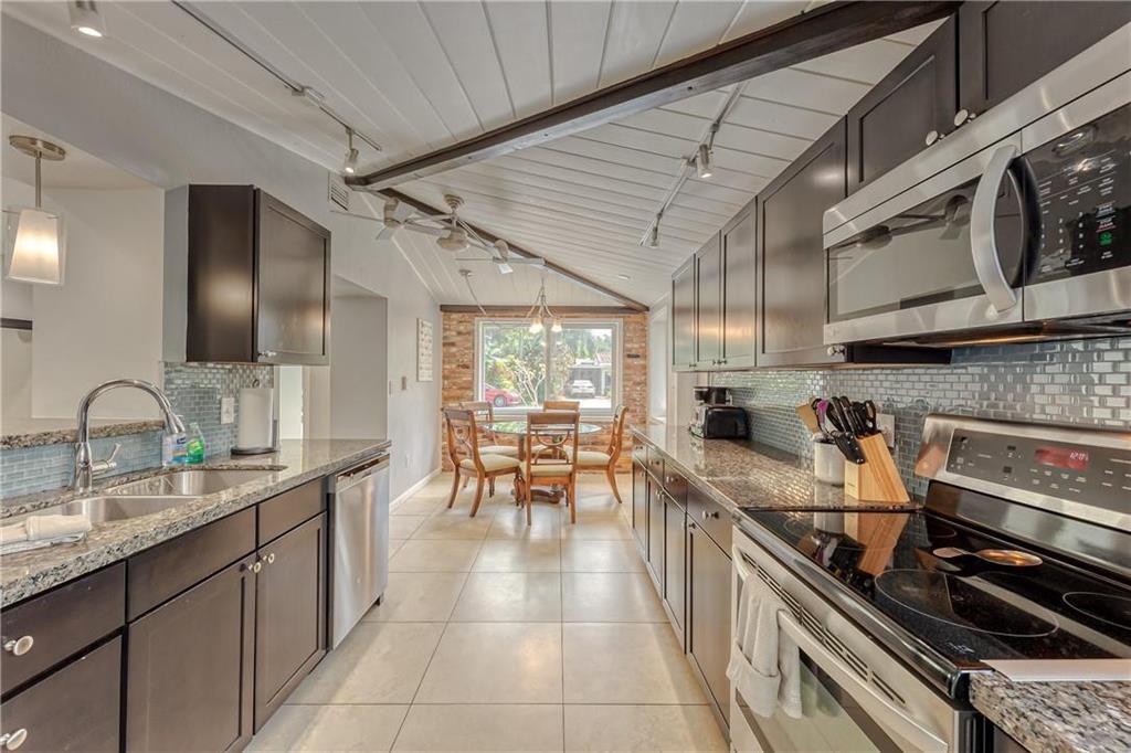Galley kitchen with dark cabinetry, granite counters, stainless appliances, and a dining table by the window.