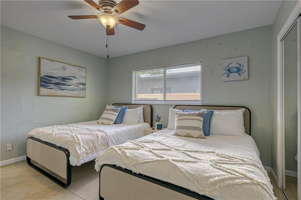 Bedroom with two white-covered beds, a ceiling fan, and mirrored closet doors.
