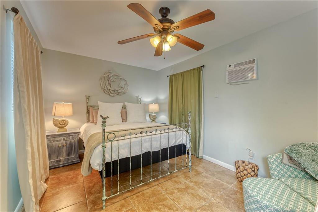 Bedroom with a white bed, decorative metal frame, ceiling fan, and tiled floor.