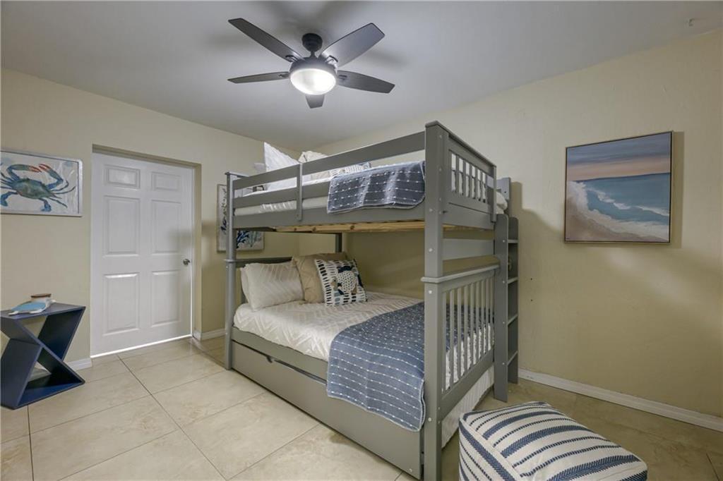 Bedroom with a gray bunk bed, blue-and-white bedding, tiled floor, and coastal wall art.