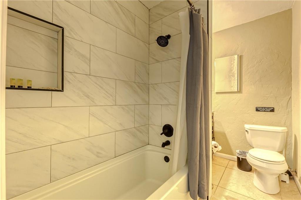 Bathroom with a marble-look tiled tub and shower, black fixtures, and a gray curtain.