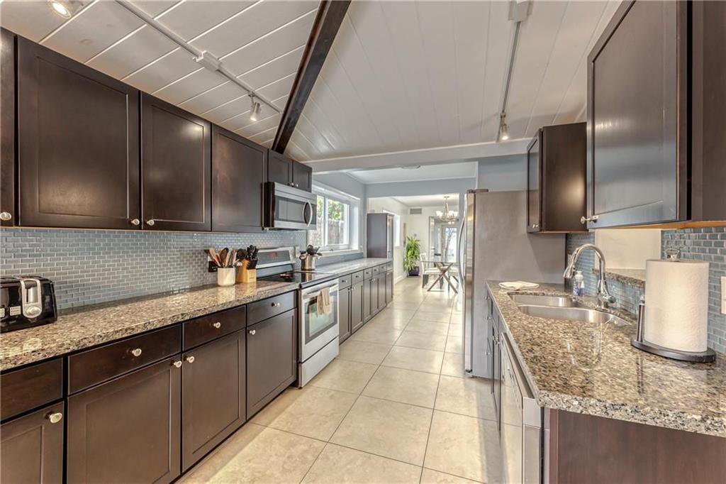 Galley kitchen with dark wood cabinets, granite counters, and a white paneled ceiling with exposed beams.