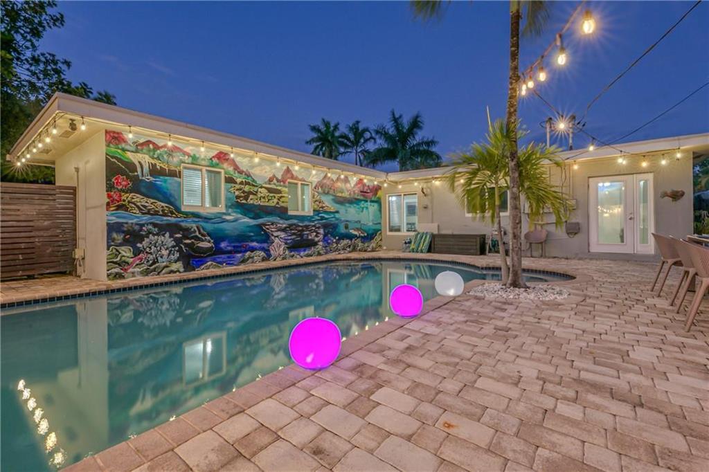 Backyard pool beside a patio with string lights, tropical landscaping, and a colorful underwater mural.