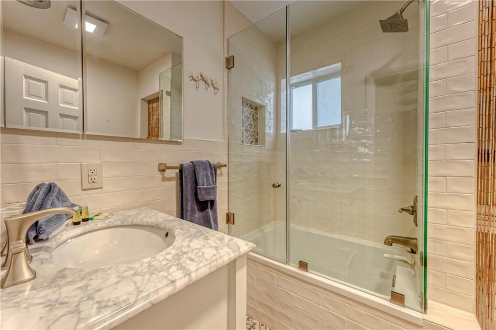 Bathroom with a marble-pattern vanity, oval sink, and glass-enclosed bathtub and shower.