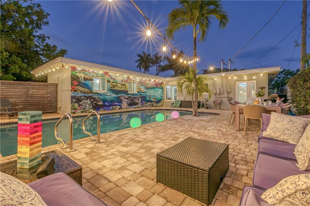 Backyard pool beside a colorful mural, furnished patio, and glowing string lights at dusk.