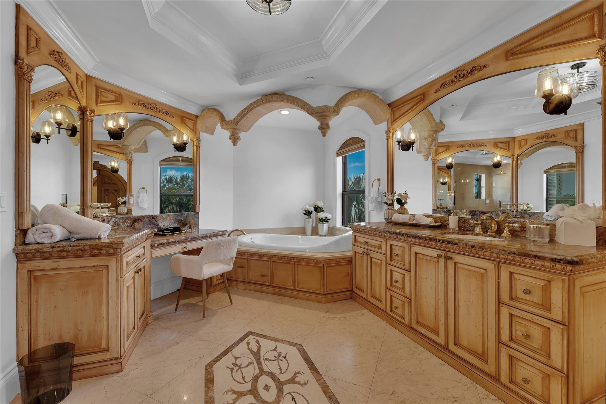 Bathroom with a soaking tub, ornate carved wood vanities, arched mirrors, and a patterned marble floor.
