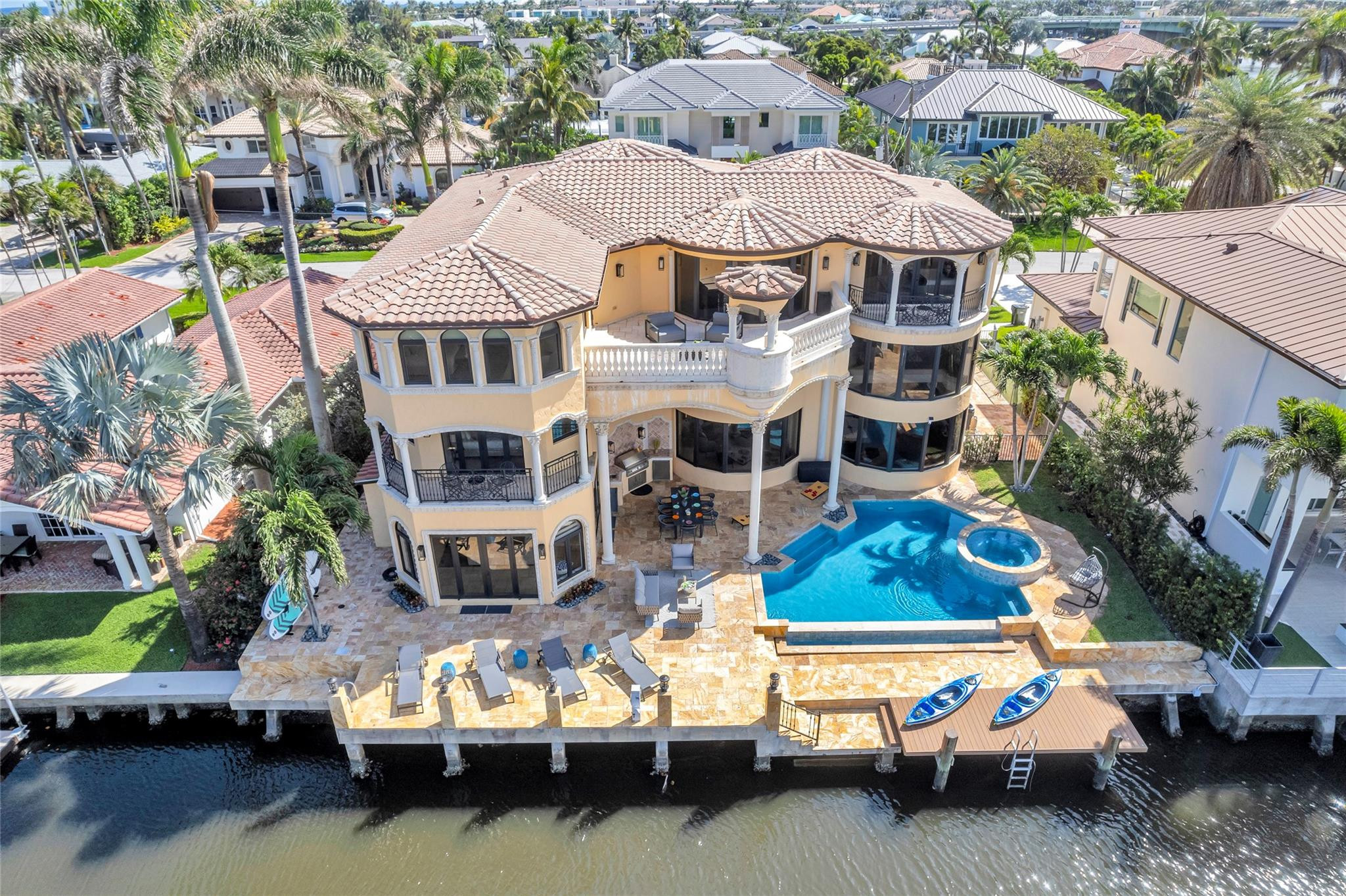 Aerial view of a waterfront home with a pool, raised spa, and dock with two kayaks.