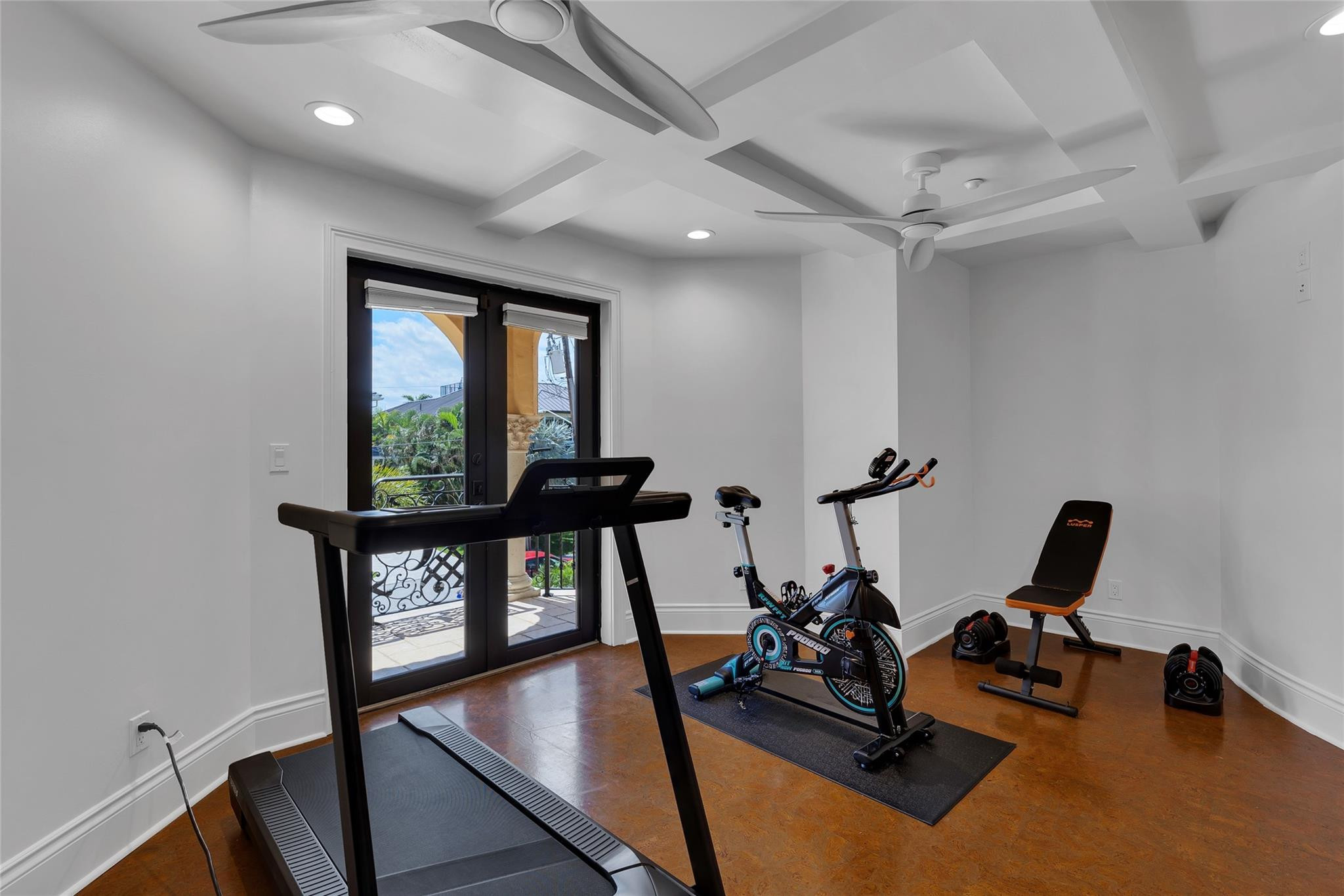 Home gym with treadmill, exercise bike, weight bench, and glass doors opening to a balcony.