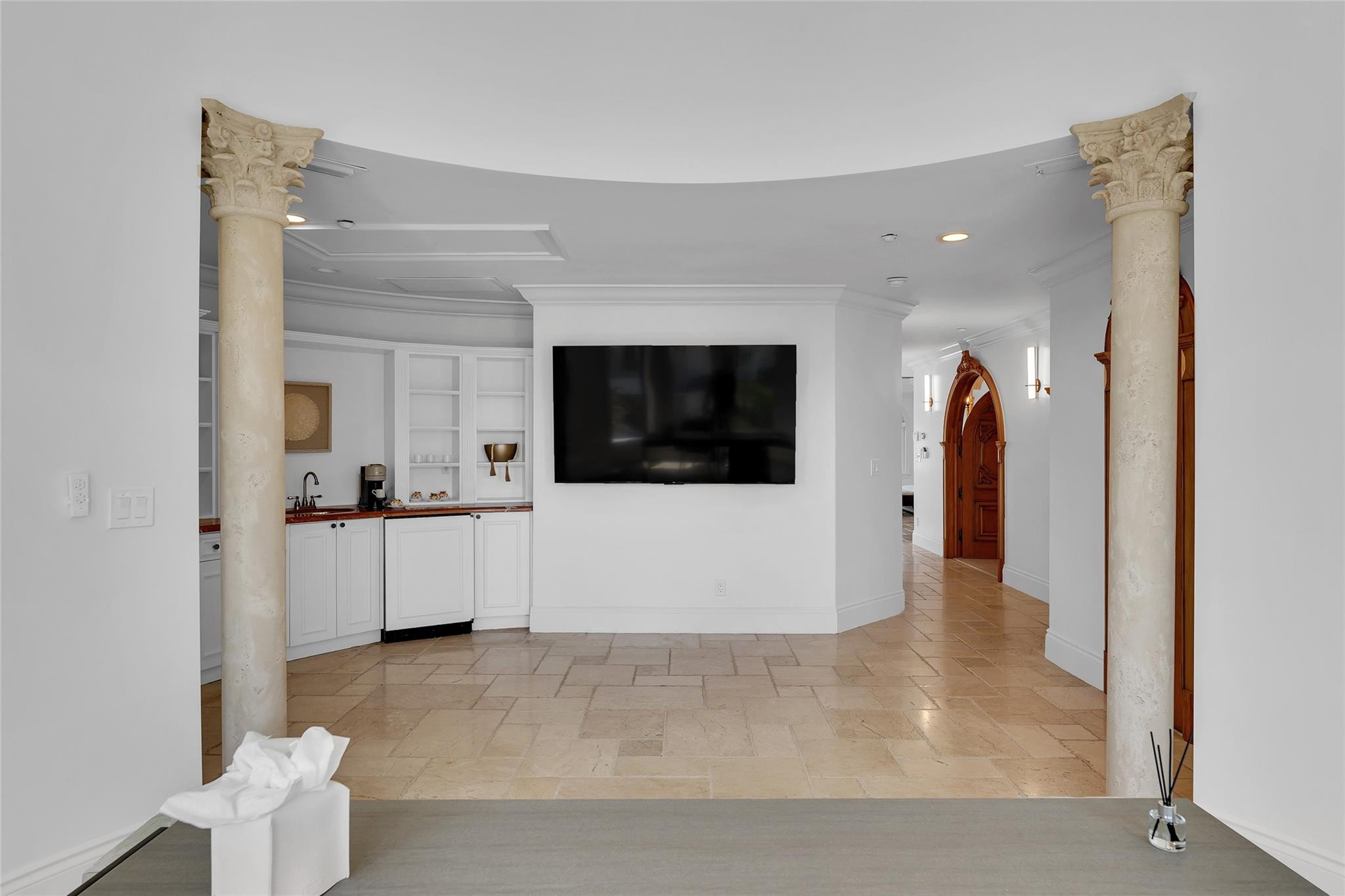 Bright interior with ornate stone columns, a wall-mounted television, built-in bar, and tiled floors.