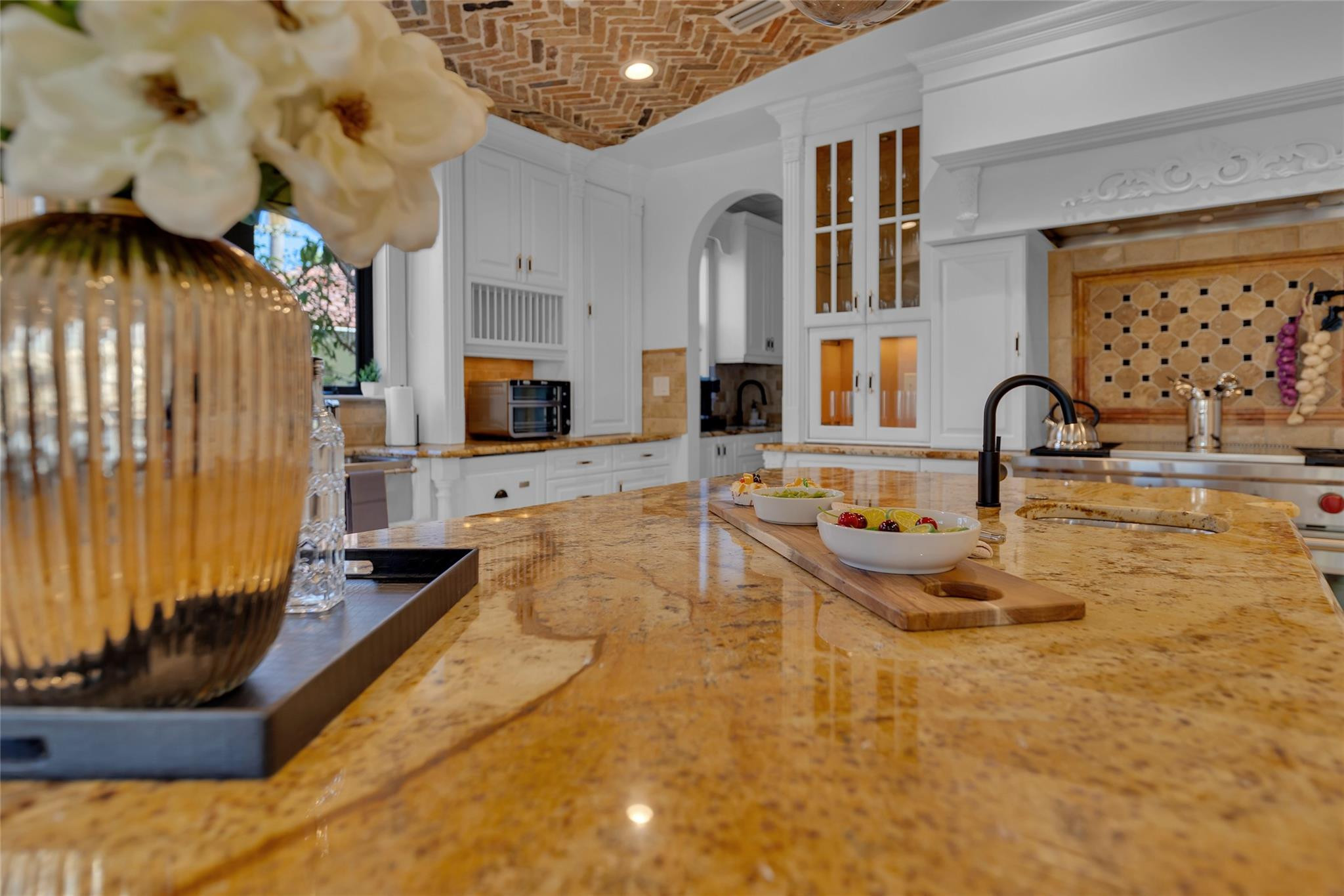 Kitchen with a granite island, white cabinetry, brick ceiling, and tiled backsplash.