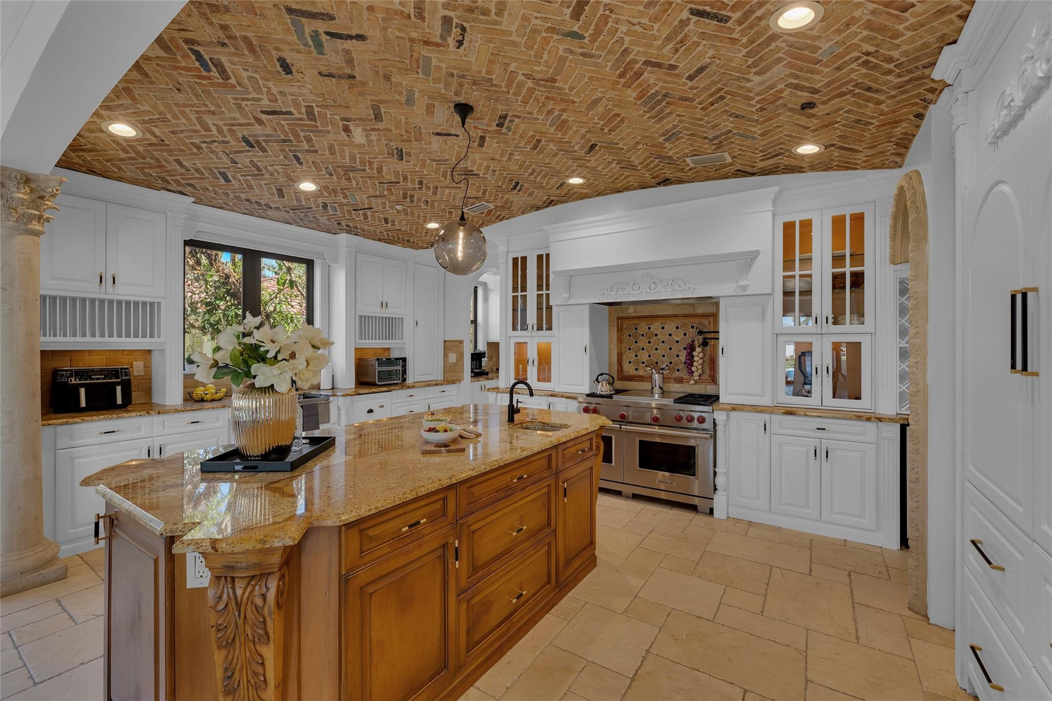 Kitchen with a carved wood island, golden stone countertop, and exposed brick ceiling.