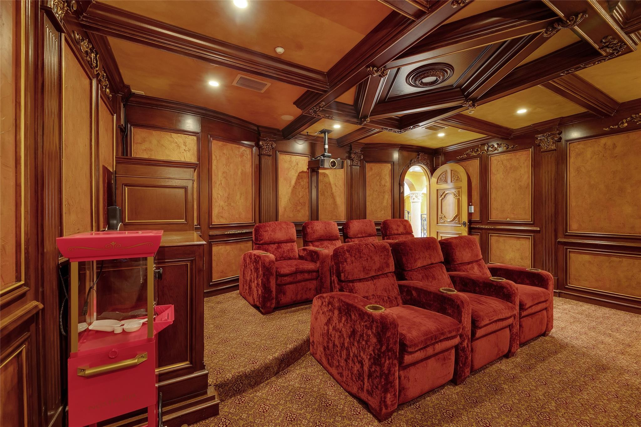 Home theater with red recliners, ornate wood paneling, a ceiling projector, and a pink popcorn machine.