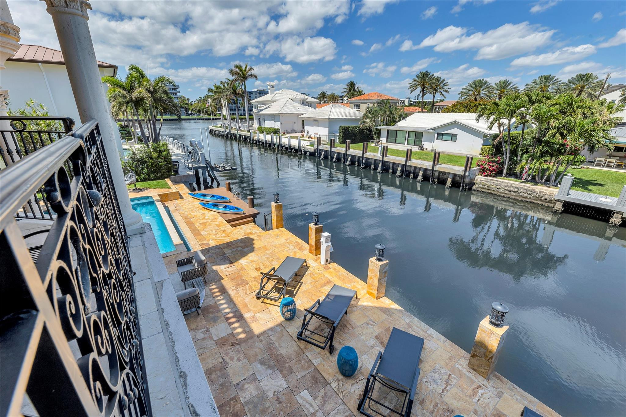 Waterfront patio with lounge chairs and a small pool overlooking a palm-lined canal.