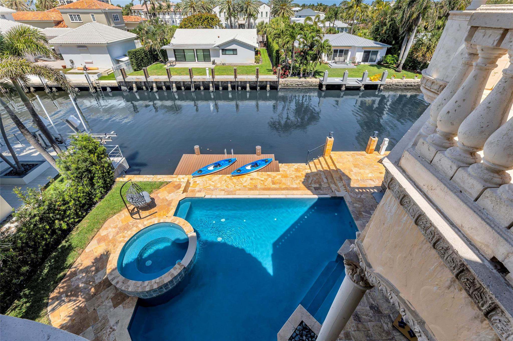Waterfront pool and attached spa overlook a canal, with two kayaks at the dock.
