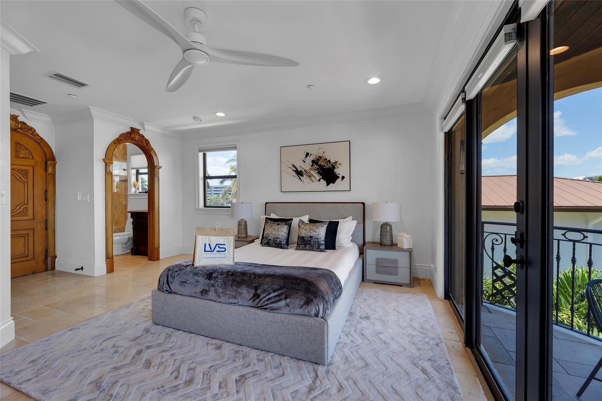 Bedroom with a gray bed, ornate wood doorway, and sliding doors to a balcony.