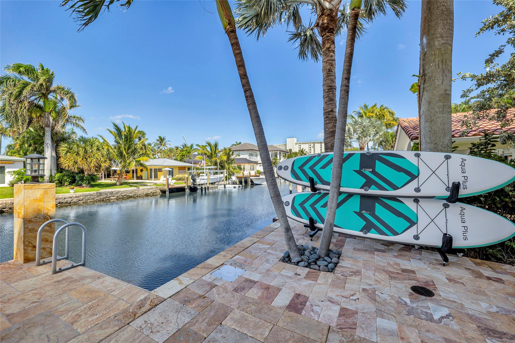 Waterfront patio beside a canal, with two turquoise paddleboards and palm trees.