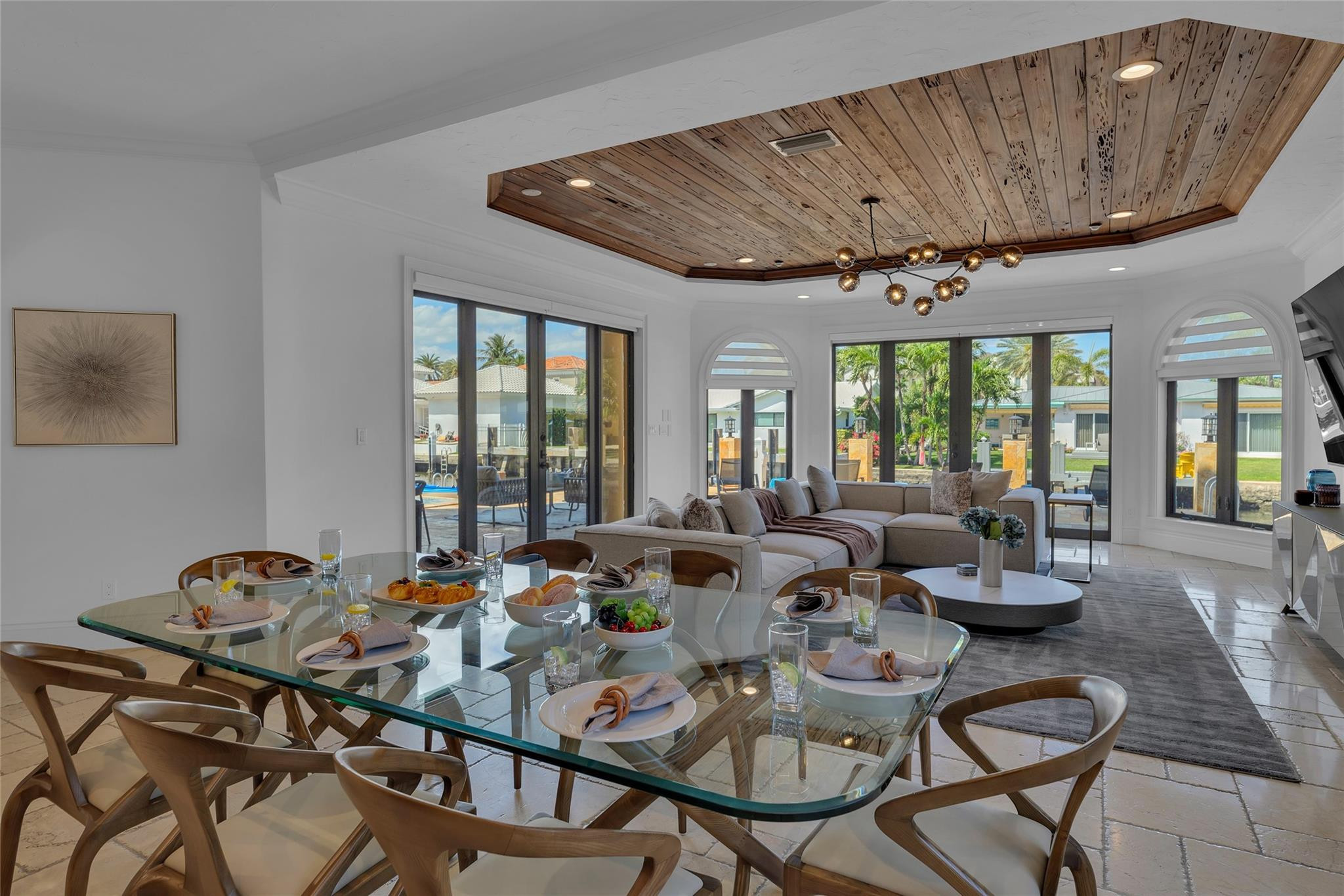 Open-plan living and dining room with a wood-plank ceiling and views through large windows.