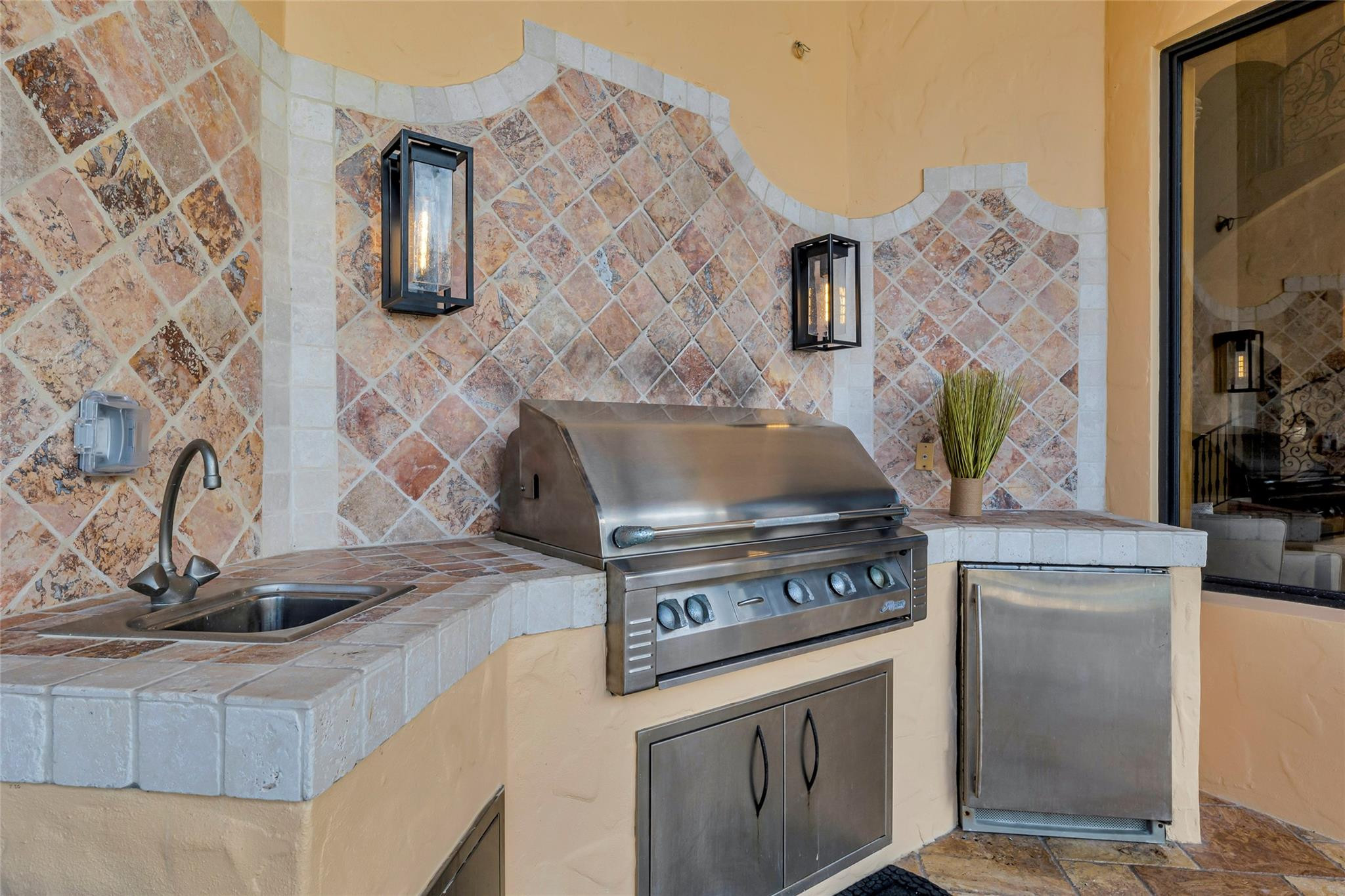 Outdoor kitchen with stainless-steel grill, sink, refrigerator, and patterned tile backsplash.