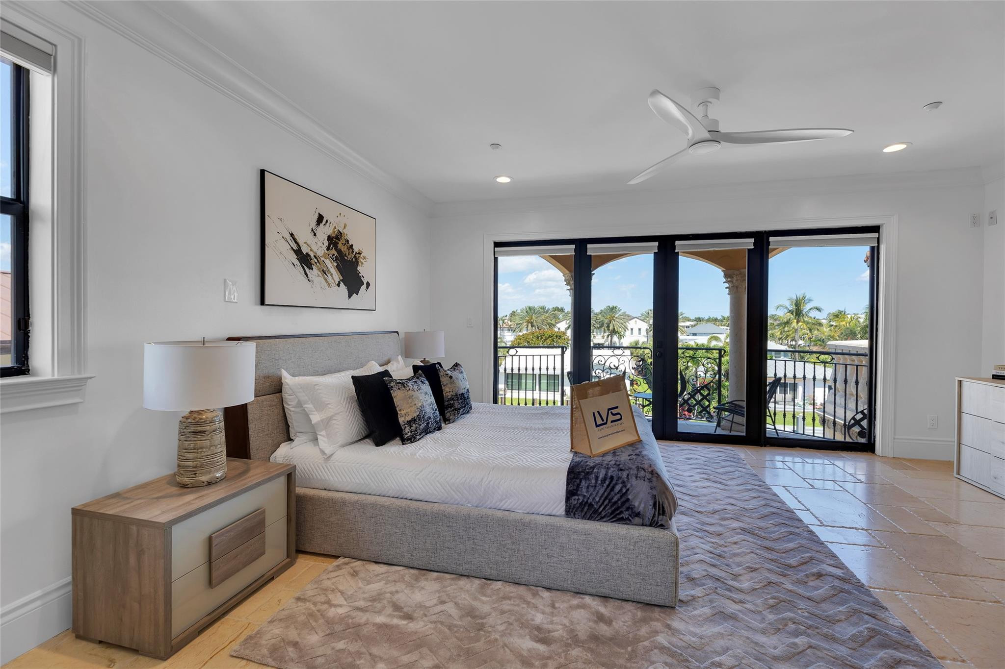 Furnished bedroom with a large bed and black-framed doors opening onto a balcony.