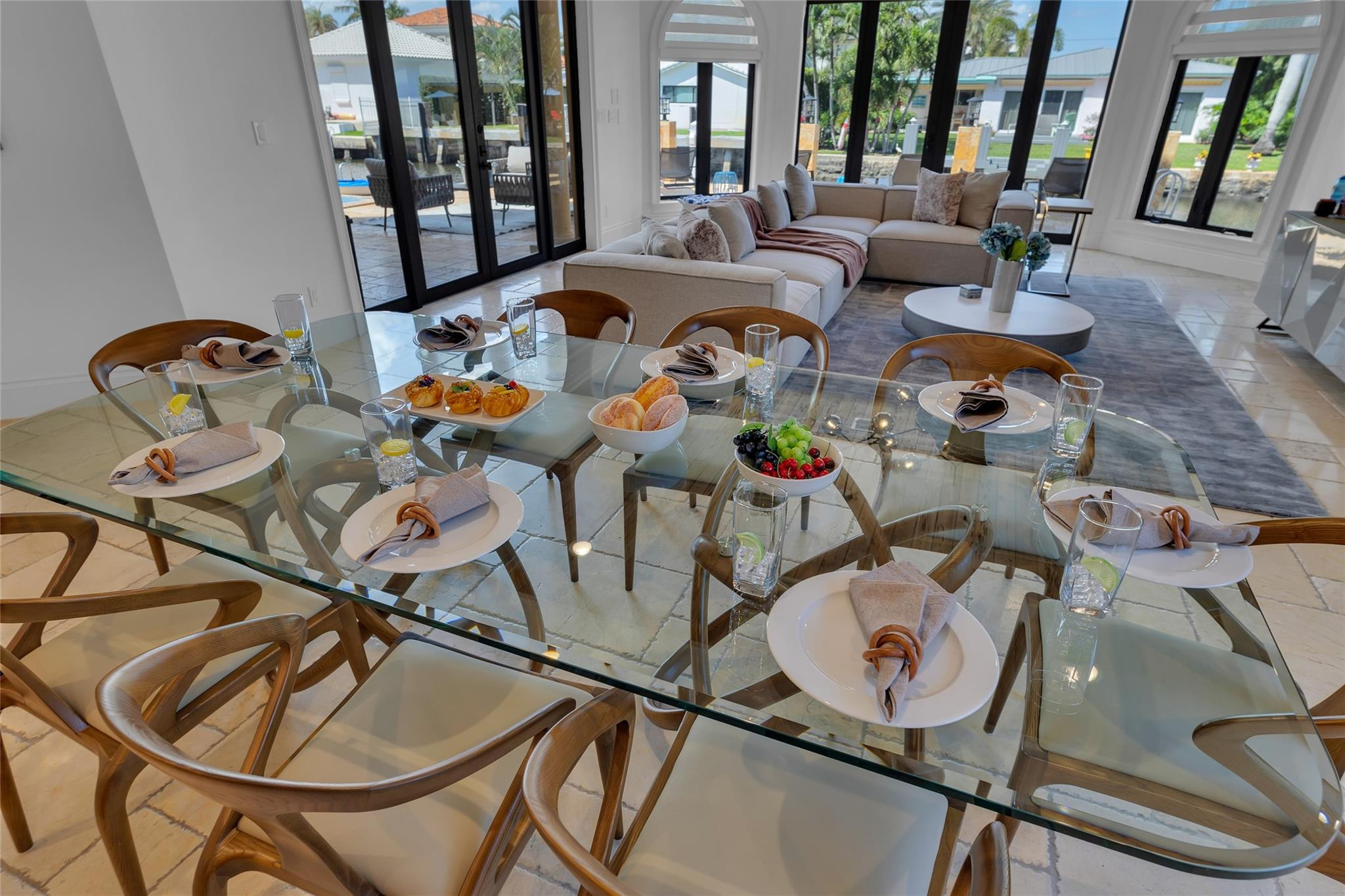 Staged dining room with glass table, adjoining living area, and canal visible through windows.