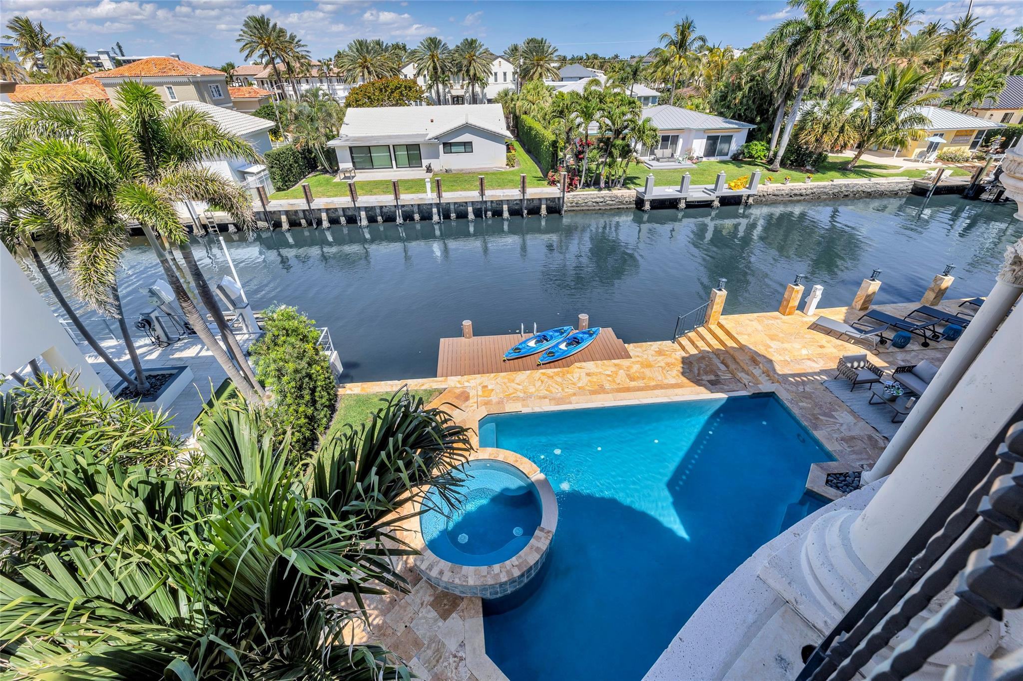 Aerial view of a canal-front pool and raised spa, with kayaks on the dock.