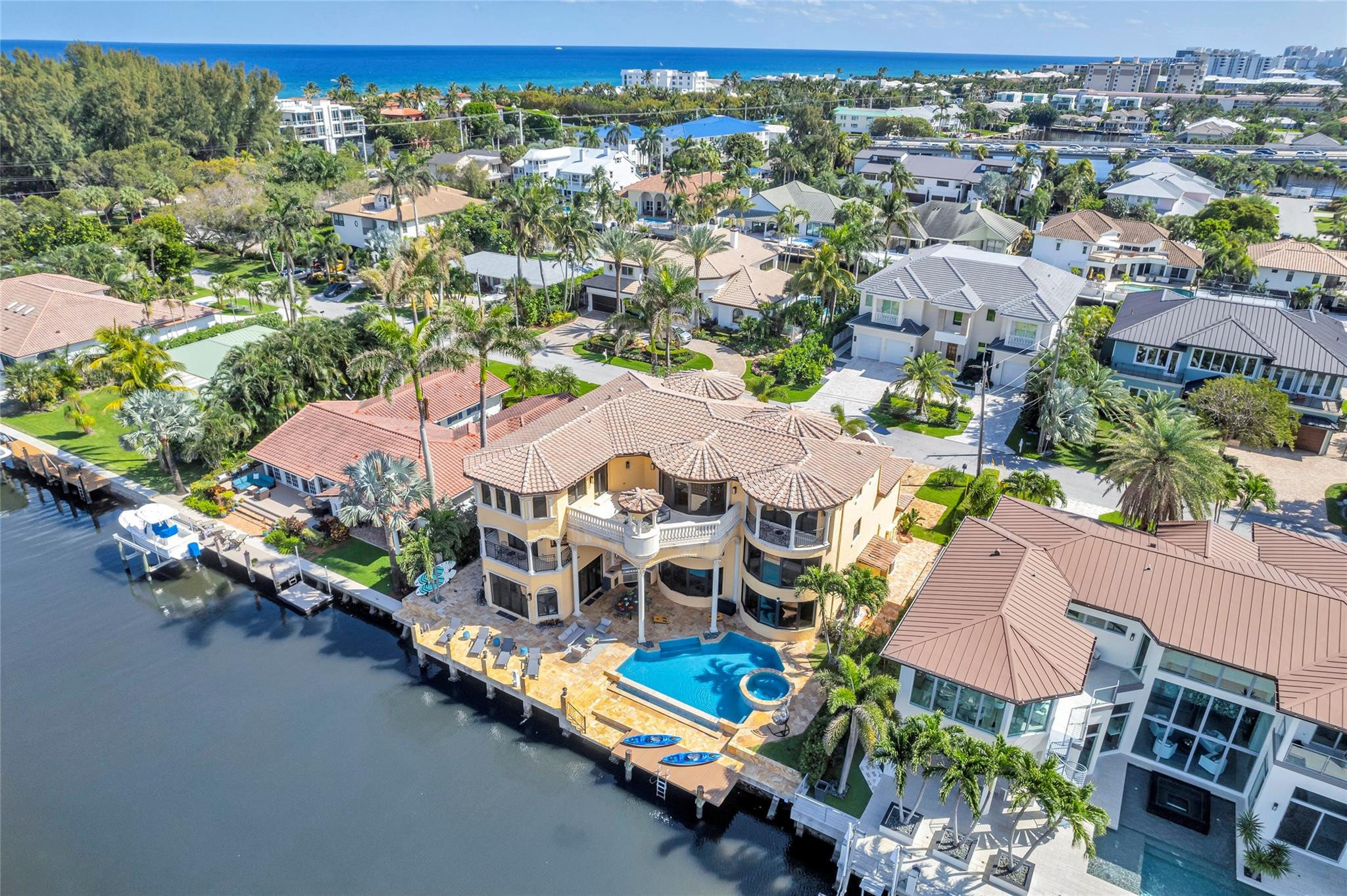 Waterfront home with a pool and dock, viewed from above with the ocean in the distance.