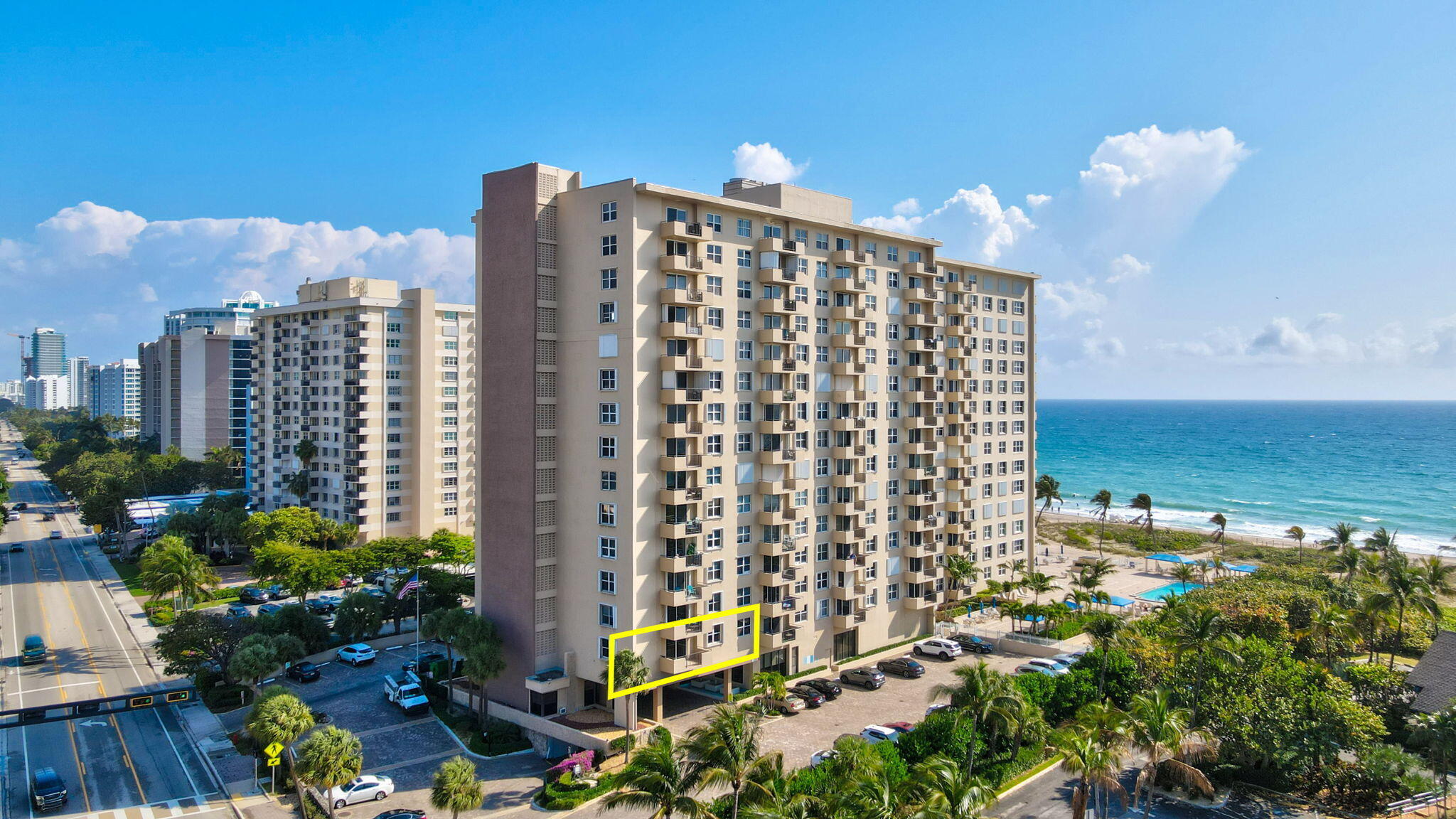 Beachfront condominium building with a yellow outline around a lower-floor unit, ocean and beach beside it.