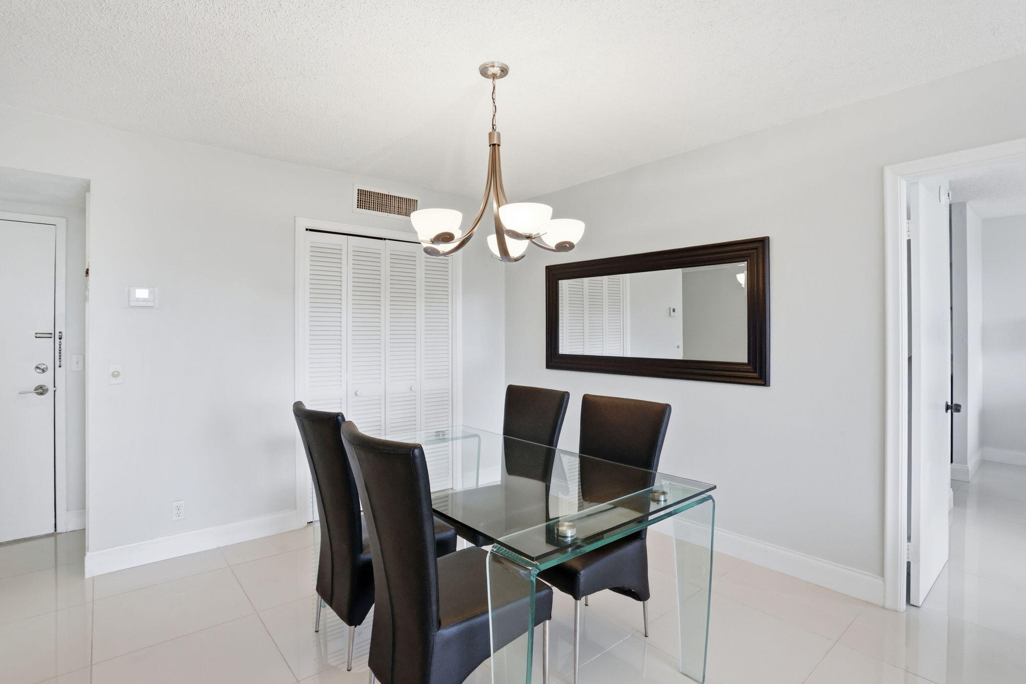 Furnished dining room with a glass table, dark chairs, and a modern chandelier.