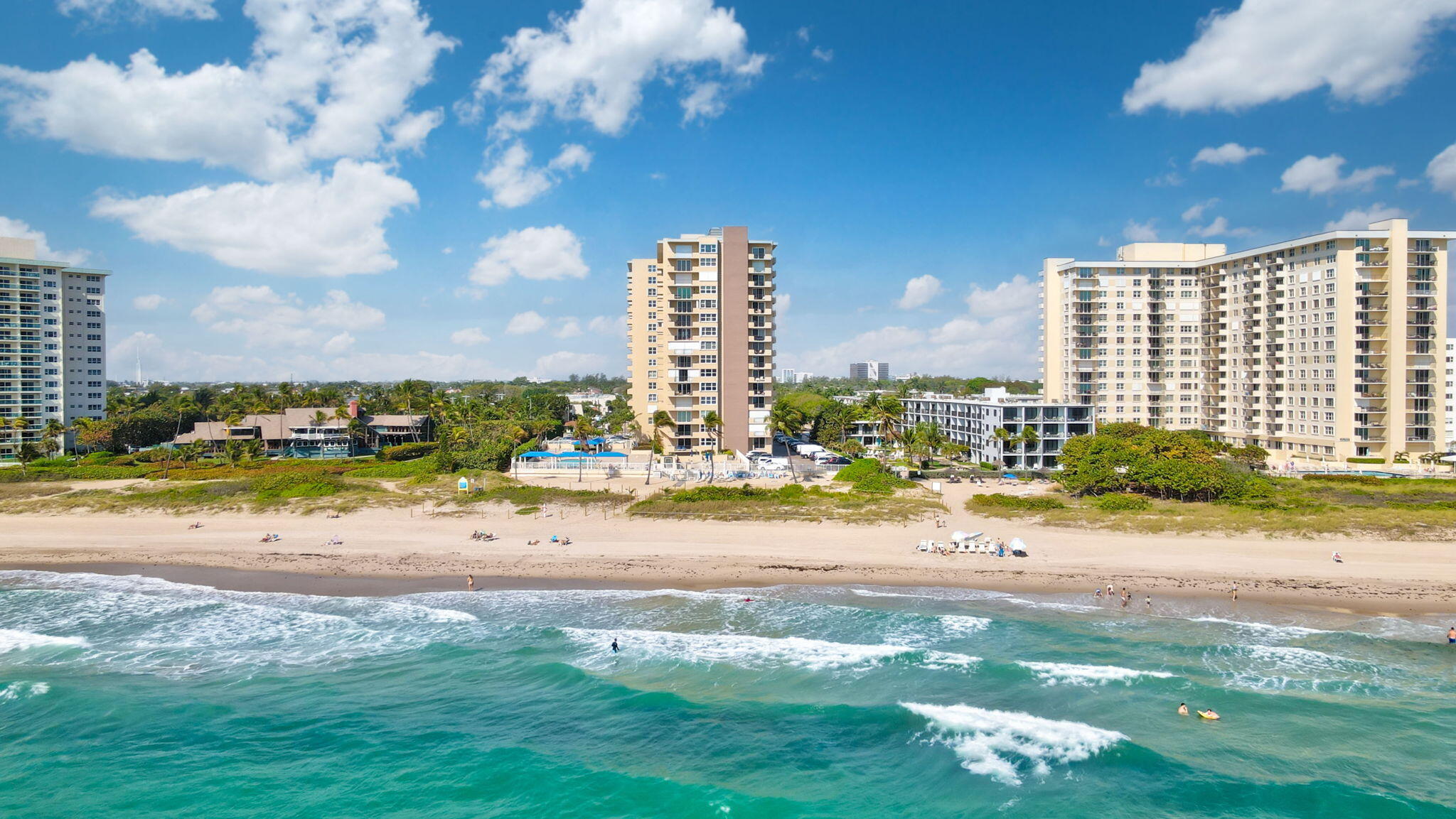 Beachfront condominiums beside a broad sandy beach and turquoise ocean.