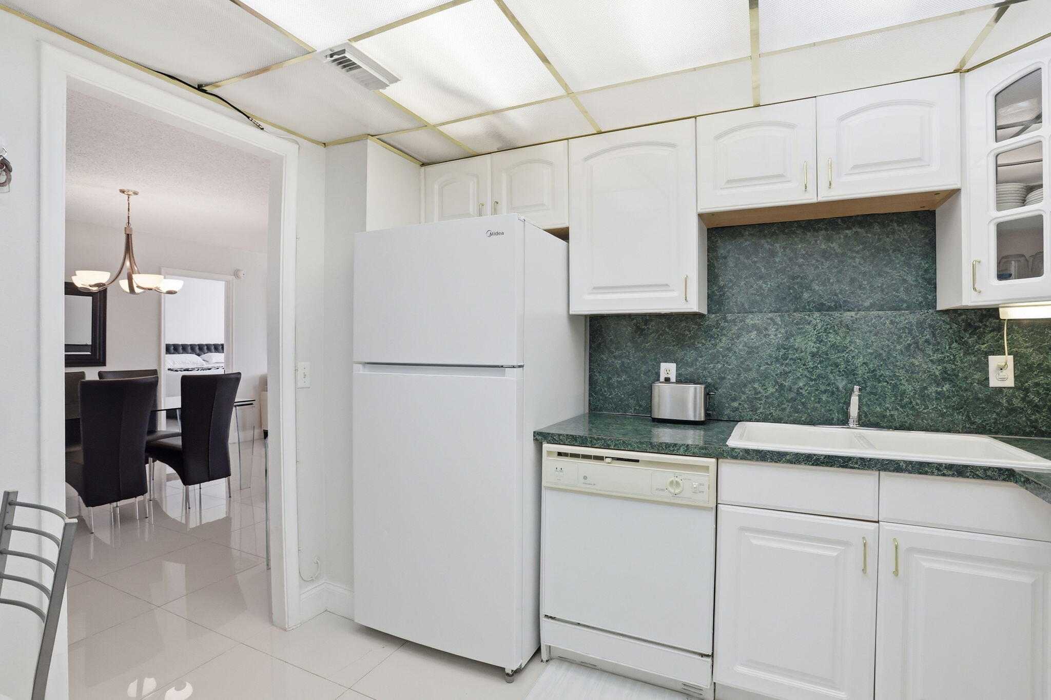 Kitchen with white cabinets, green counters and backsplash, and a refrigerator beside the dining area.