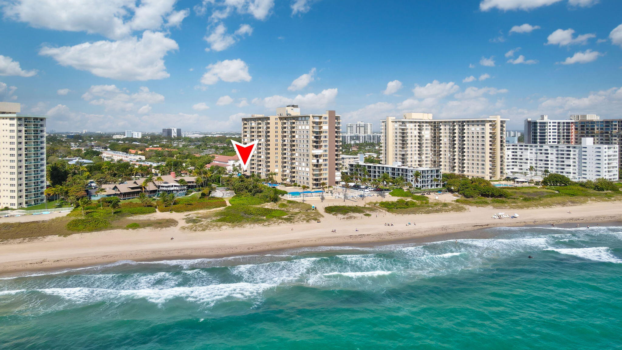 Beachfront condominium tower marked by a red arrow, overlooking the sandy shore and turquoise ocean.