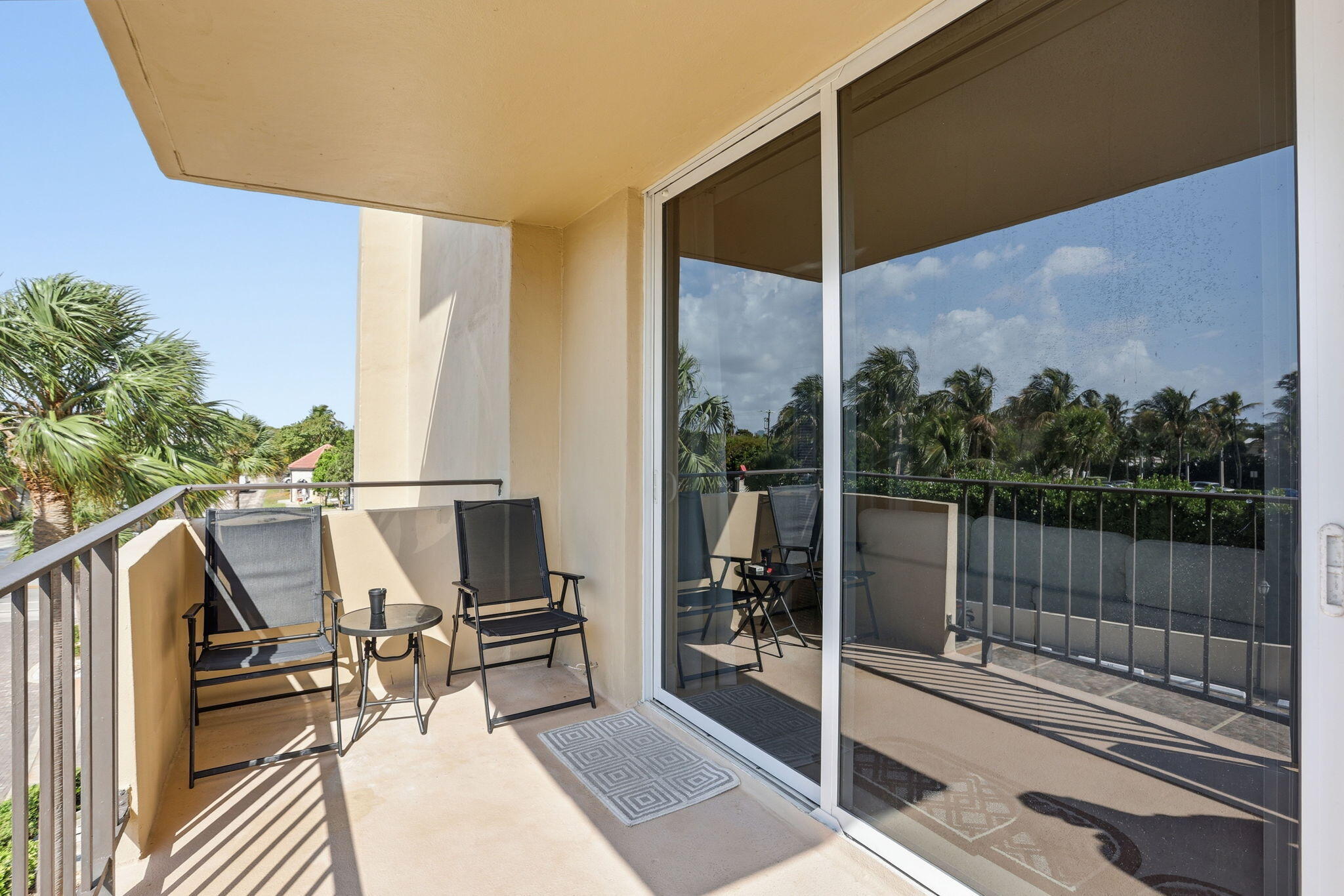 Apartment balcony with two chairs and a small table beside reflective sliding glass doors.