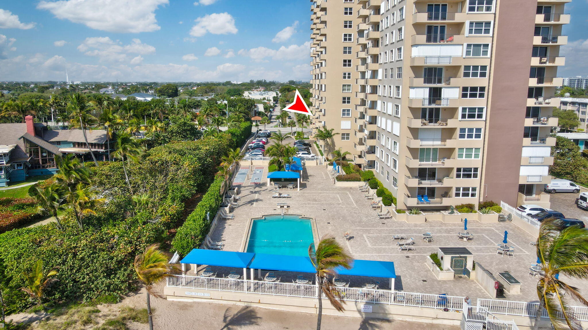 Aerial view of a condominium tower with a pool and a red arrow pointing toward the building.
