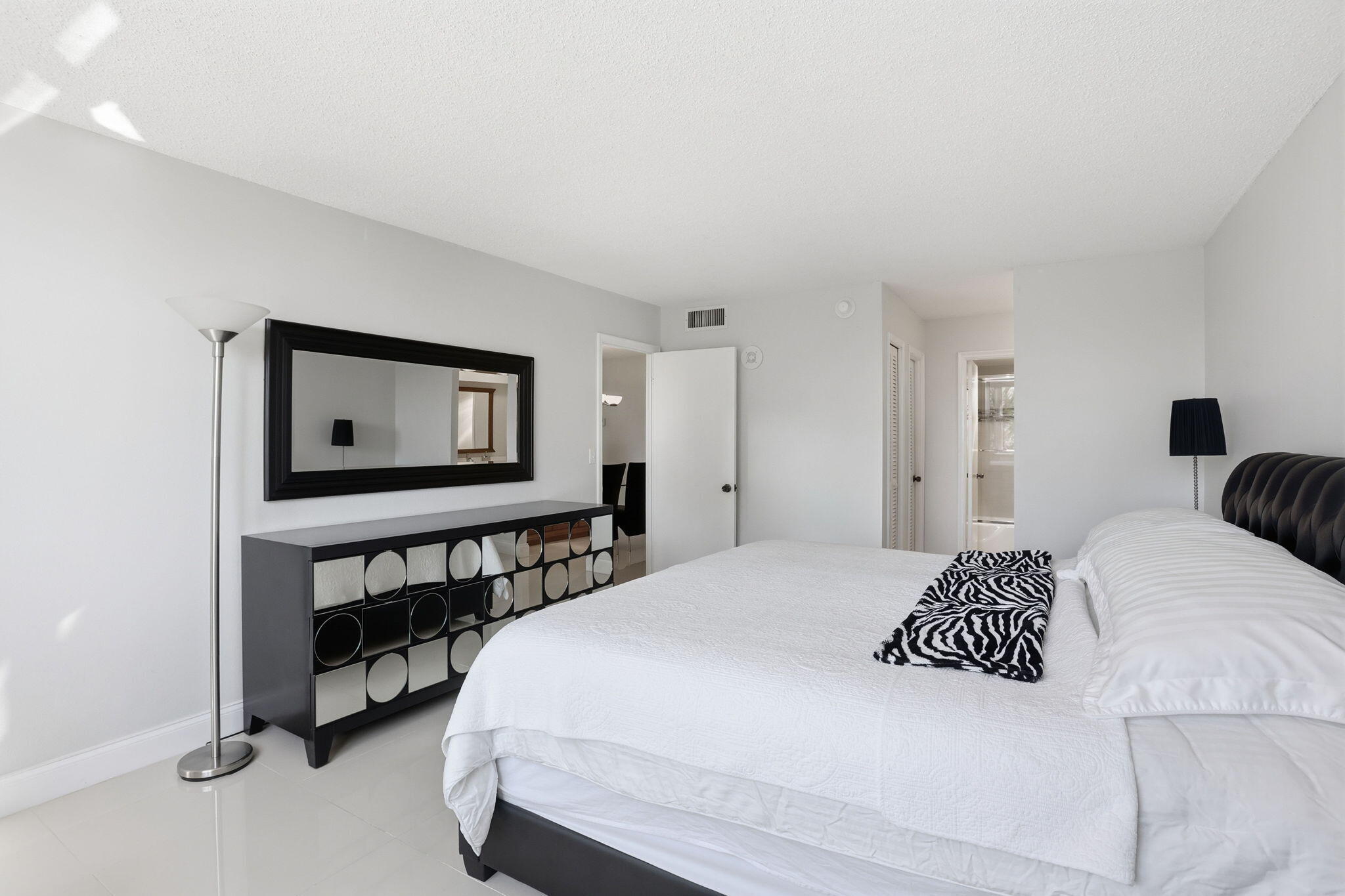 Bright bedroom with a white bed, black tufted headboard, and geometric-front dresser.