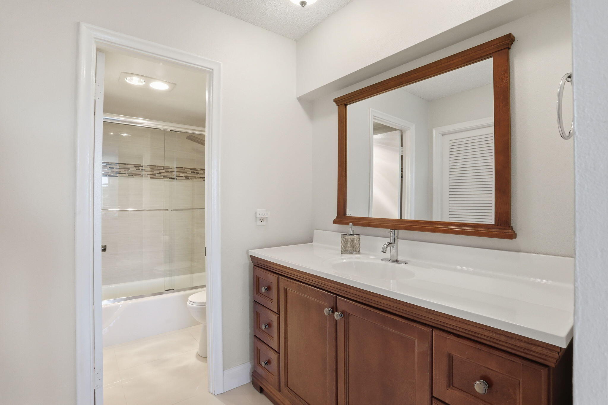 Bathroom with a dark wood vanity and framed mirror beside a glass-enclosed tub and shower.