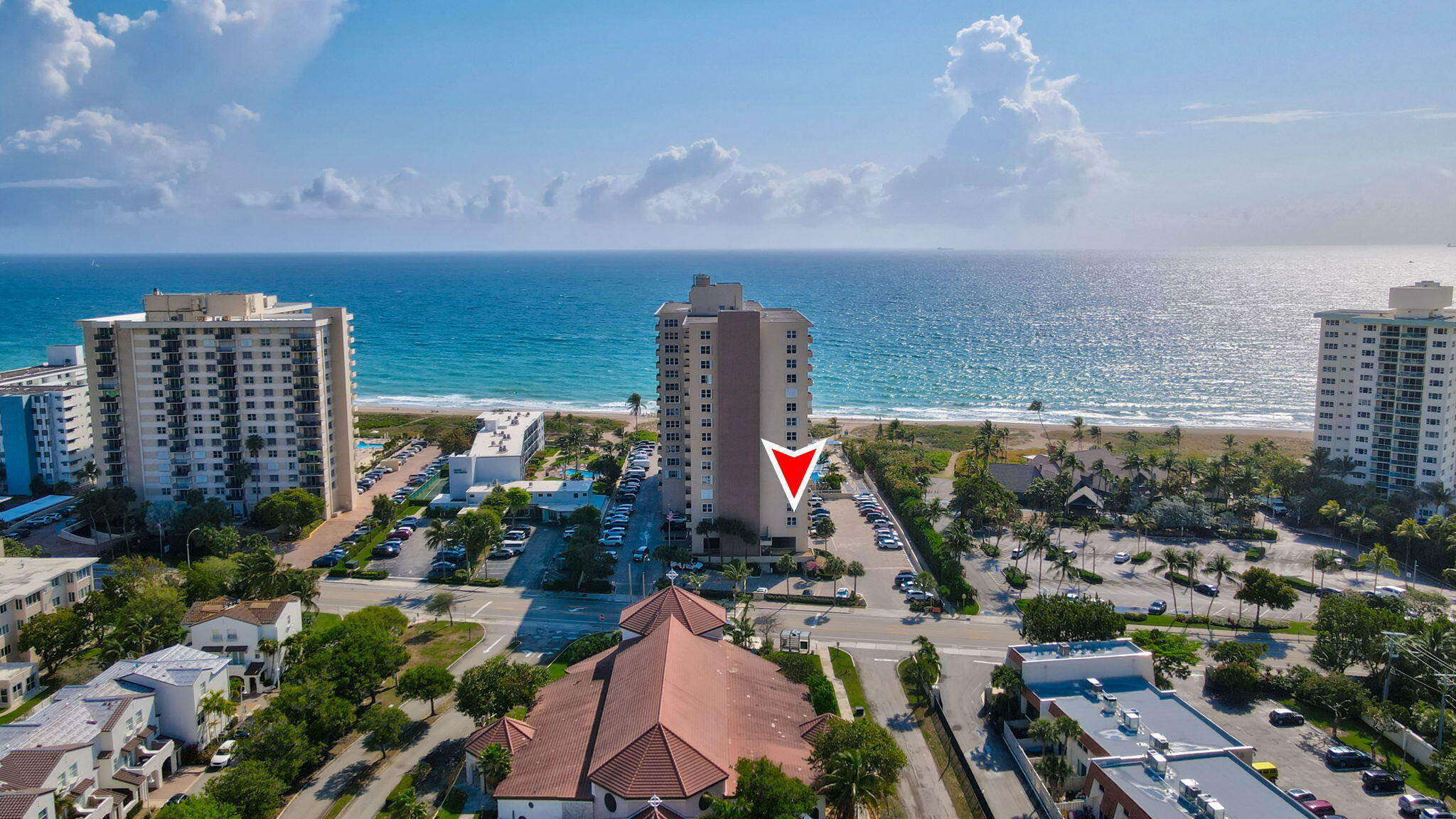 Aerial view of beachfront condominiums, with a red marker pointing to the central tower beside the ocean.