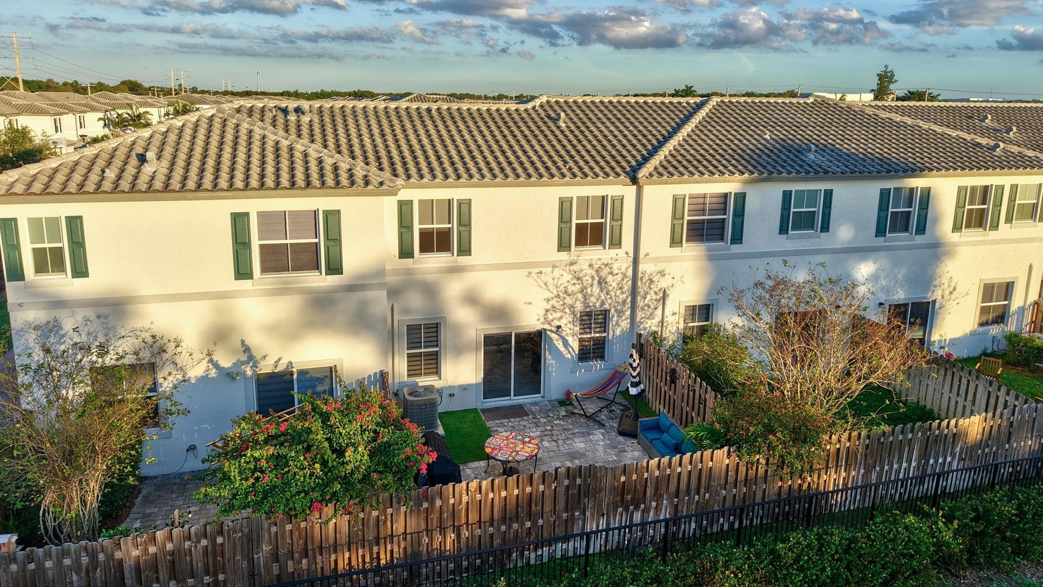 Townhouse rear with green-shuttered windows, fenced patio, and tiled roof in warm evening light.
