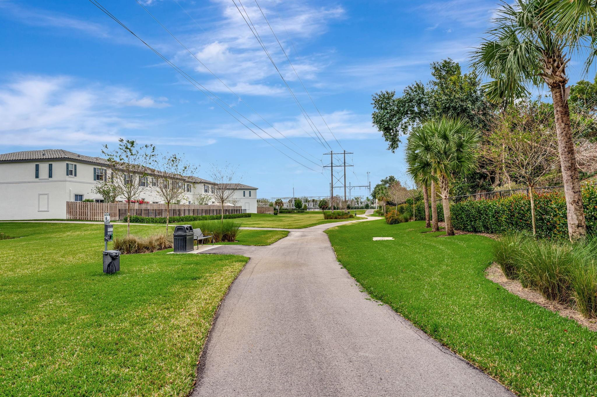 Community walking path bordered by lawns, palms, and neighboring homes.
