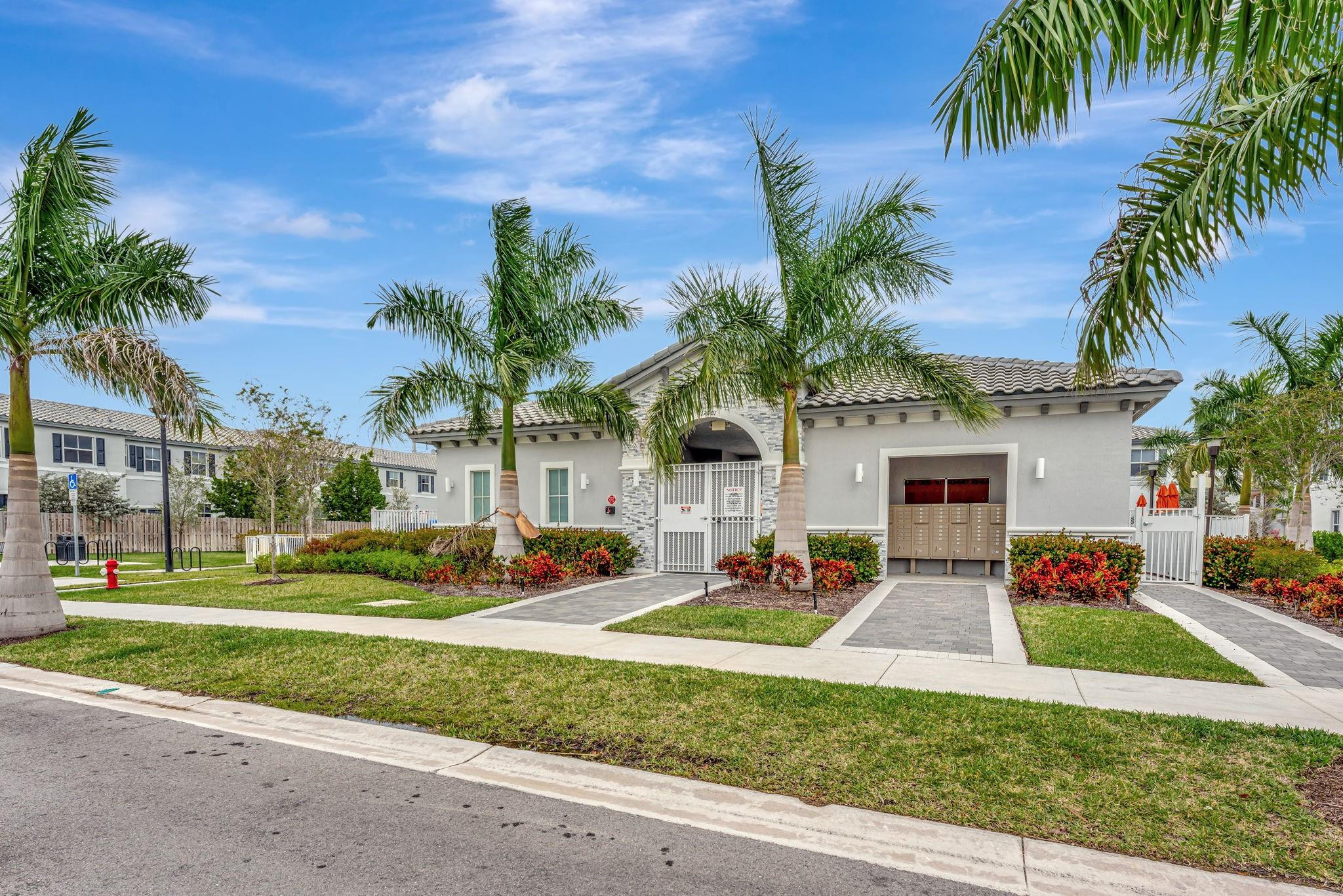 Gray tiled-roof building with a gated entrance, mailbox bank, and palm trees.